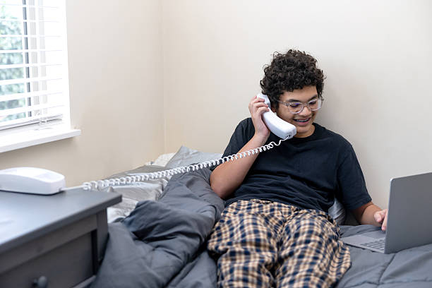 Stock photo at home of a teenage boy using a handheld landline telephone in his bedroom.