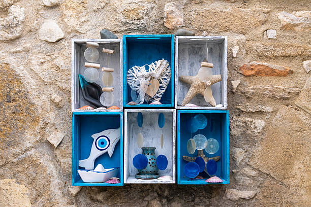 Marine themed still life with wooden boxes containing decorative boat, fish, seashells placed against textured stone wall. Copy space for text. Nautical background in rustic style.