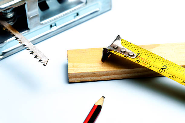 Jigsaw blade, yellow measuring tape, and pencil on wood plank, representing carpentry, diy, and building concepts