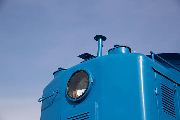 A bright blue train engine stands tall against a clear sky during early morning hours. The details of its structure are highlighted, showcasing its vibrant color and design.