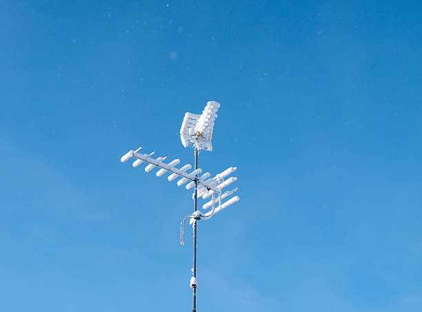 Television antenna covered with snow against clear blue sky