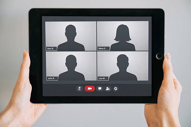 Close-up of hands holding a tablet displaying a video conference interface with silhouette avatars and generic names. Clean, commercial-ready mockup ideal for remote work, online meetings, and digital communication concepts.
