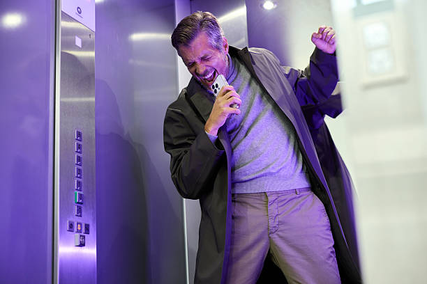 Cheerful male entrepreneur having fun while singing on smart phone during his ride in an elevator.