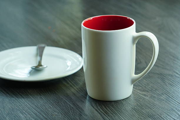 A white ceramic mug with a vibrant red interior sits next to a small plate.