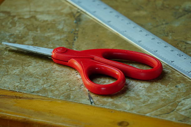 The red scissors and the metal ruler are lying on the marble surface.