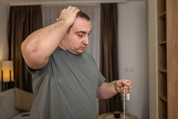 Man holding a measuring tape, looking disappointed with his weight and health