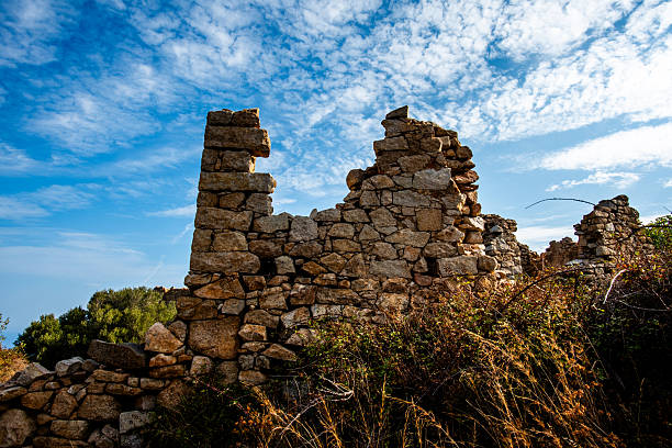 Ruined stone walls and partial structures in Sant'Antonino, Corsica, France, surrounded by vegetation and photographed under a textured sky for history and travel themes.