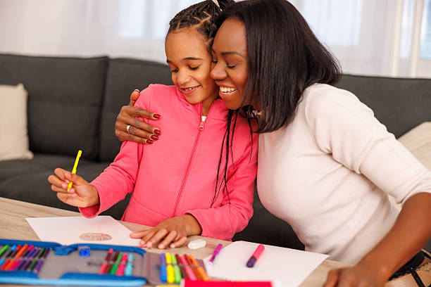 Mid adult mother helping elementary school daughter with art homework, little girl making a drawing for art class