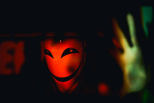 Person wearing a scary orange smiling mask in a shadowy environment
