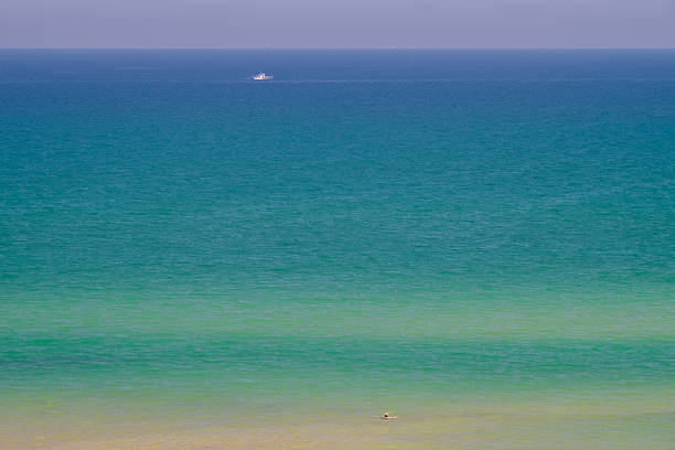 A beautiful calm seascape with different shades from blue to green with a fishing boat and a silhouette of a person swimming. Bliss scene.