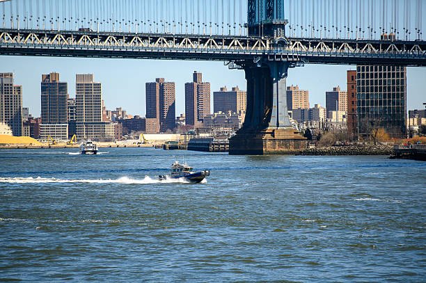 Boat sailing under Manhattan Bridge in daylight. A small boat sails along the river under the Manhattan Bridge in daylight.