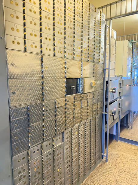 A row of secure metal safe deposit boxes lines the interior wall of a modern bank vault corridor, with strong lighting emphasizing the metallic doors and security features. This financial security scene is ideal for banking advertisements, wealth management concepts, insurance marketing, and editorial content about savings, investments, or asset protection.