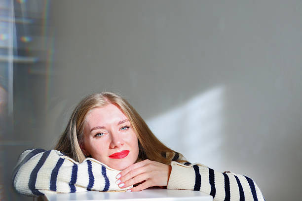 Thoughtful blonde woman with red lips relaxing indoors, copy space. High quality photo