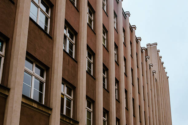 Modern urban building facade with repetitive vertical columns and rows of windows, minimalistic architectural perspective under cloudy sky.