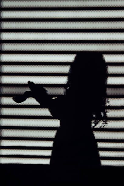 Expressive girl silhouette with hand gestures in dramatic striped window shadow. Freedom and creativity concept.