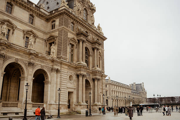 Paris, France – February 8, 2026: Visitors walking through the historic Louvre Museum courtyard surrounded by elegant classical architecture.