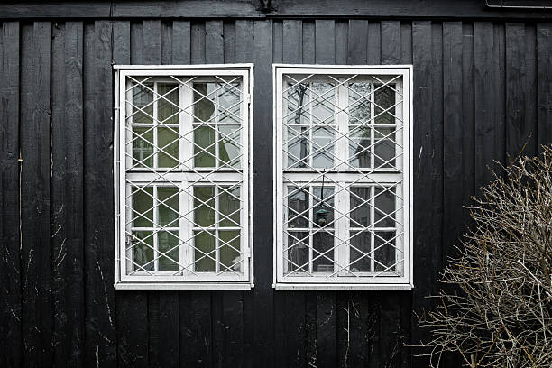 White lattice windows on dark wooden house facade with strong contrast and geometric symmetry, minimalist architectural detail and textured exterior wall.