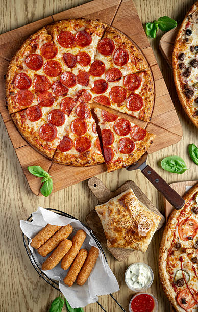 Delicious pepperoni pizza served with breadsticks and dipping sauces. Pepperoni pizza with a slice removed sits on a wooden board next to breadsticks and sauces.