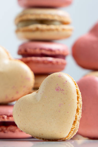 A Delightful Heart-Shaped Macaron Sits Gracefully in Front of an Enticing Arrangement of Vibrant, Stacked Macarons at a Charming Pastry Shop, Showcasing a Variety of Colors and Flavors That Are Sure to Captivate Any Dessert Lover