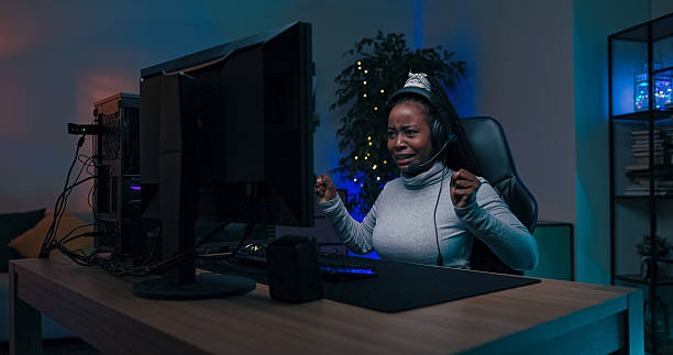 A young woman in a headset shows despair after defeat in a multiplayer shooter. She quickly refocuses on the game, holding her backlit mouse and keyboard, talking to teammates.