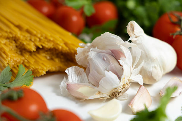 Fresh tomatoes are arranged with garlic and uncooked spaghetti on a kitchen counter, ready for cooking.