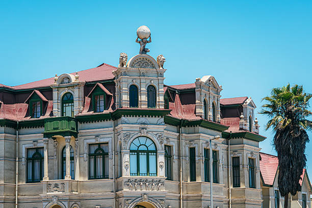 Ornate historic building facade in Swakopmund, Namibia, featuring colonial architecture, decorative sculptures, a red roof and palm tree against a bright clear blue sky on a sunny day.