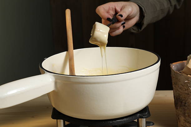 Une personne prépare une fondue bourguignonne au fromage dans un récipient. Elle utilise une cuillère en bois pour mélanger le fromage fondu et trempe un morceau de pain dans le mélange.