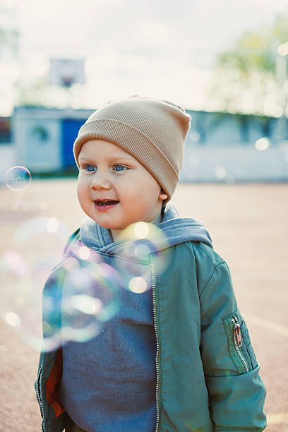 Toddler boy running outside with soap bubbles. Child on a warm spring day for a walk in a jacket and hat.