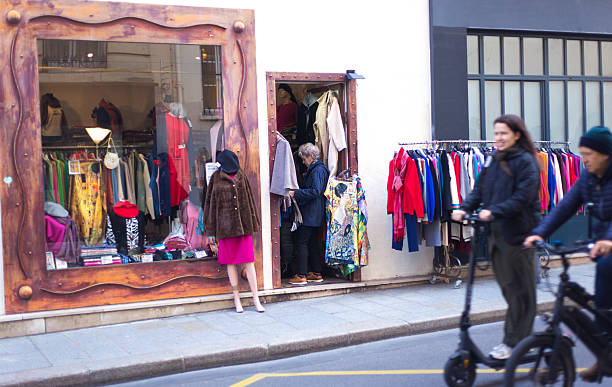 Paris, France - October 17, 2025: A senior woman shops in a clothing boutique in the Marais as two people whiz by on electric scooters.