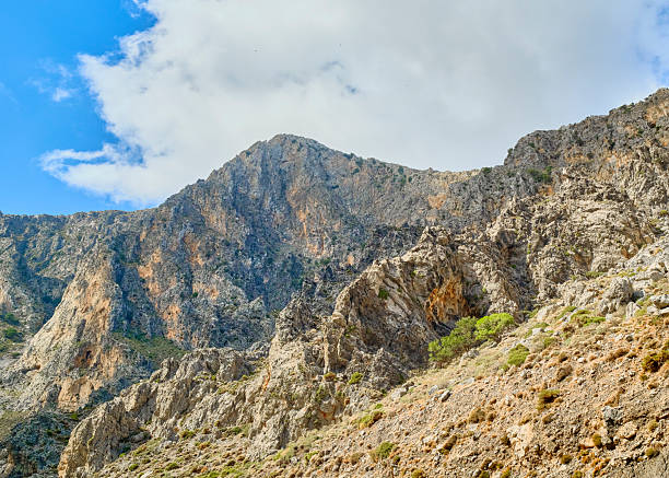 The island of Crete: landscape Crete  showcases rugged mountains, rocky hills, and an arid hillside beneath a bright blue sky with white clouds. This natural outdoor scene highlights Greek terrain and scenery, perfect for travel, nature, tourism, and adventure stock projects celebrating Crete and Greece.