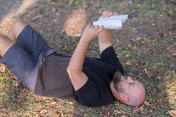 Hispanic man with a beard in his 40s lying on the couch reading a book, he is very comfortable with the heat of a pellet stove.