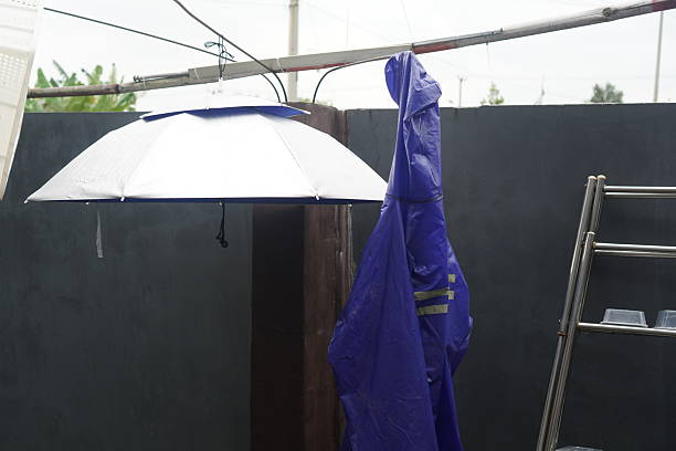 A still life shot of a blue raincoat and a silver umbrella hanging side by side on a clothesline. This image captures the daily routine of preparing for the monsoon or wet season in a domestic setting.