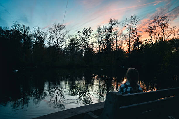 Girl sitting on a park bench observing a vibrant sunset reflecting on the lake