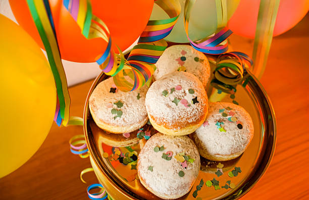 Eine Platte mit Krapfen (auch bekannt als Berliner, Pfannkuchen oder Kreppel), die mit Puderzucker bestäubt und mit Konfetti sowie Luftschlangen dekoriert sind. Dieses Gebäck ist eine traditionelle Leckerei für die Faschings- oder Karnevalszeit.