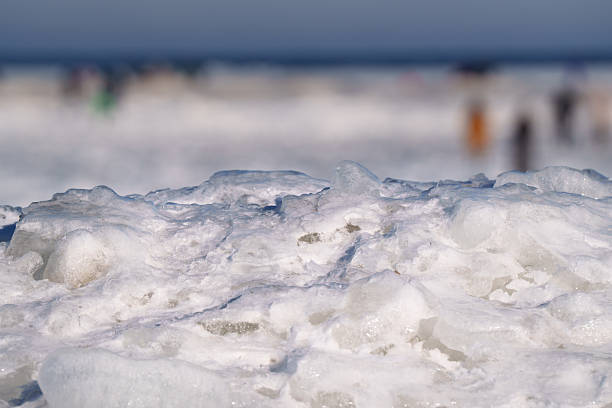 Winter Frozen Sea Texture Background. Close view Poland Europe showing crystalline ice formations, layered frozen water surface, soft blue tones, shallow depth blur silhouettes distant shoreline. Minimal natural pattern suitable wallpaper, seasonal design, cold climate concept.