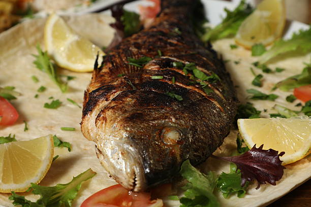 Raw mackerel and whole fish fillets are arranged on a kitchen counter next to a stovetop, featuring parsley sprigs in containers and on a platter, ready for a healthy homemade meal