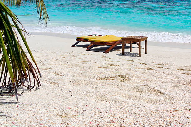 Two wooden beach chairs and a table standing in the sand on tropical beach inf front of turquoise water