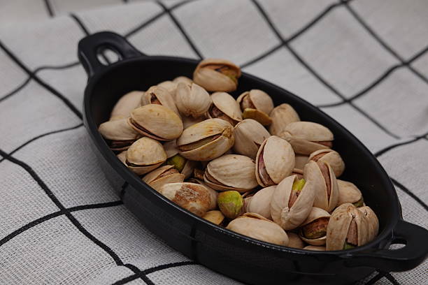 Roasted pistachios overflowing a dark bowl placed on a checkered tablecloth, creating a tempting snack presentation