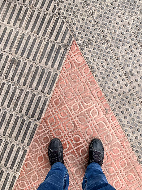 High angle close-up view of person standing next to tactile paving used on sidewalks to assist individuals with visual impairments in navigating urban environments in the city of Valencia, Spain