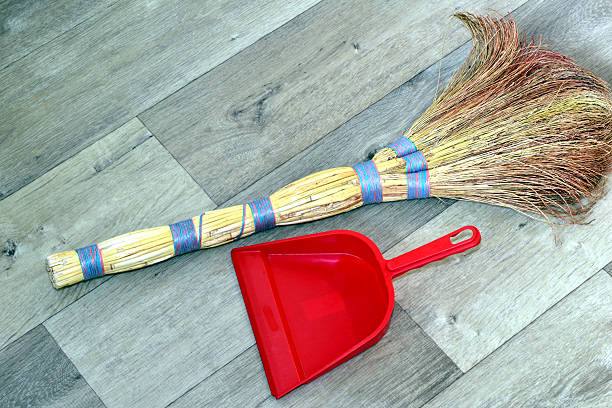 A millet broom and a plastic dustpan for manual trash removal lie on the floor. View from above.