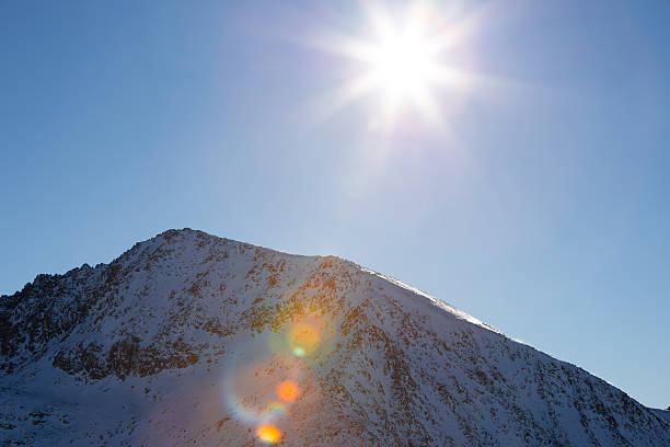 Bright sun over snow covered mountain peak in clear blue sky. High quality.