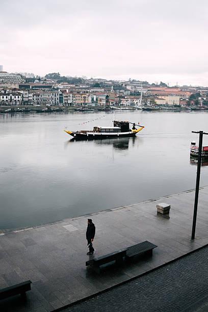 Man standing alone by douro river watching rabelo boat on a quiet day in porto, portugal