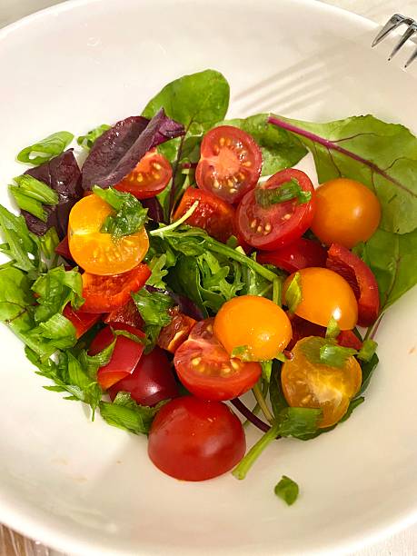Fresh vegetable salad with cherry tomatoes, yellow tomatoes and mixed leafy greens in white bowl. Healthy vegetarian food concept, clean eating, diet nutrition and organic ingredients