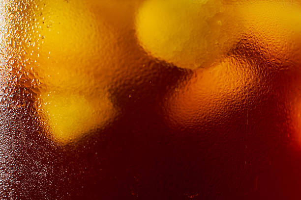 The macro lens captures the refreshing moment when iced coffee blends with ice cubes and foam in a glass, delicately showcasing the condensation droplets on the glass wall and the rich aroma of the coffee.