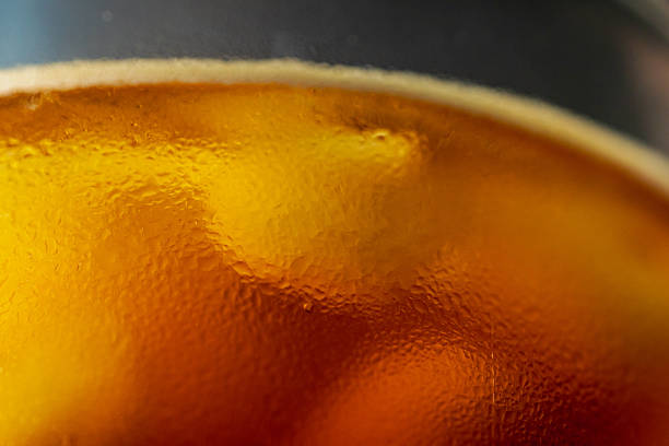 The macro lens captures the refreshing moment when iced coffee blends with ice cubes and foam in a glass, delicately showcasing the condensation droplets on the glass wall and the rich aroma of the coffee.