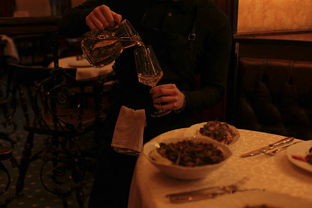 Anonymous waiter wearing gloves polishing wine glass with towel, hands and torso visible, performing restaurant worker duties in professional setting