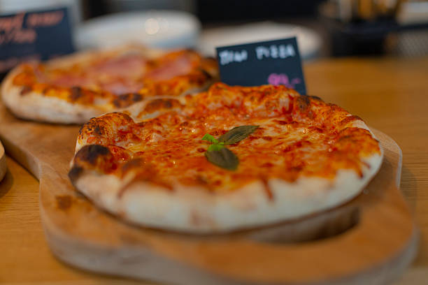 Closeup margherita pizza on board, golden crust and melted mozzarella with fresh basil, rustic pizzeria counter background, warm ambient lighting, shallow depth of field, appetizing texture and herb