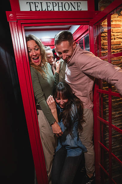 Group of friends laughing and having fun together inside a traditional british telephone booth