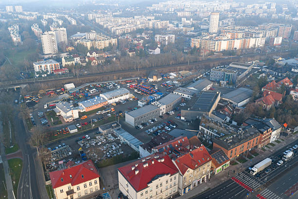 Oblique aerial view of a busy roadway with vehicles, sidewalks and landscaped public space. Contrast between traditional red-roof buildings and modern street design captured in Krakow, Poland.