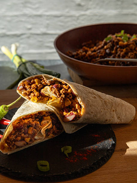 Spicy Beef Burrito Wrap Cut in Half on Slate Board with Chili Peppers